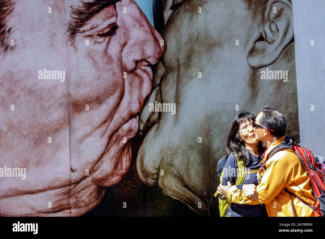 Berlin wall graffiti East Side Gallery, Asian tourists are kissing under a frightening kiss Brezhnev Honecker Germany graffiti wall Stock Photo