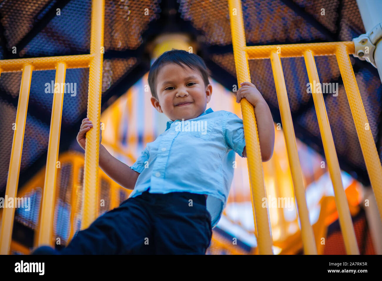 A three year old boy holding on to the rails of a childrens playground and having fun swinging his feet of the edge. Stock Photo