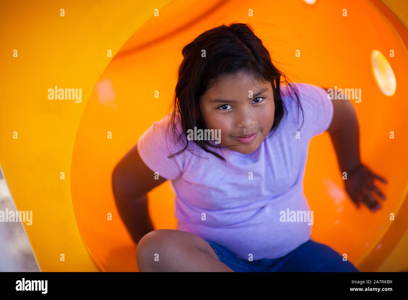 A pretty young girl getting out of a playground slide with a smile. Stock Photo