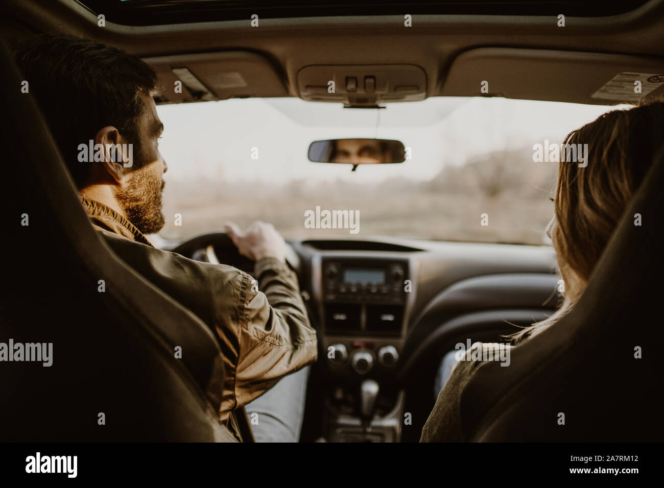 Beautiful couple doing a car trip on countryroad, view from rear seat. Stock Photo