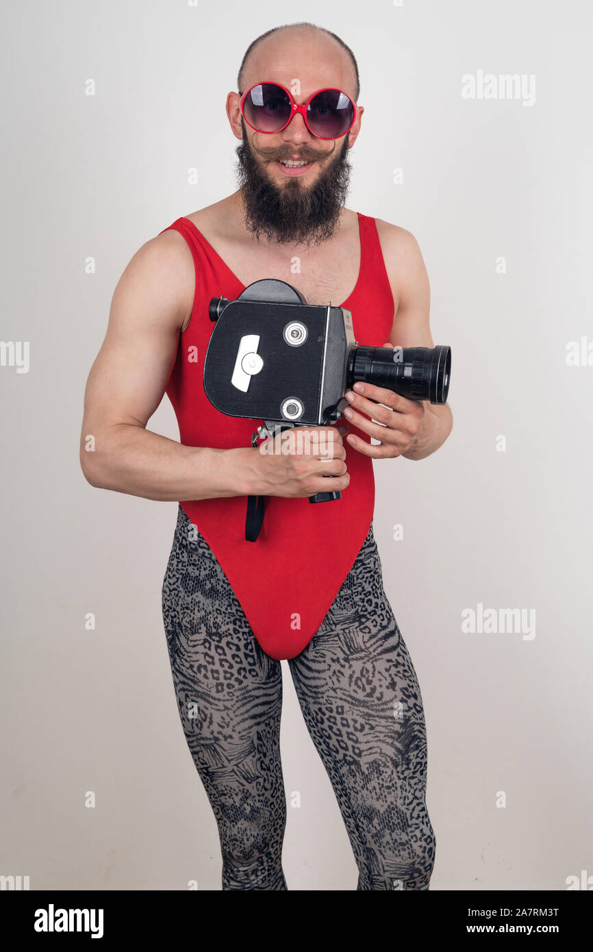Crazy guy in red bodysuit and leopard leggings posing with an old video camera in his hands Stock Photo