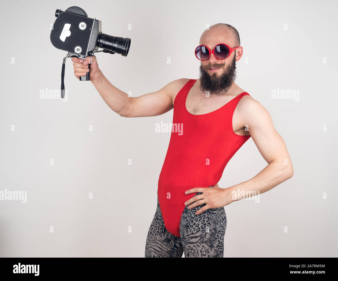 Crazy guy in red bodysuit and leopard leggings posing with an old video camera in his hands Stock Photo