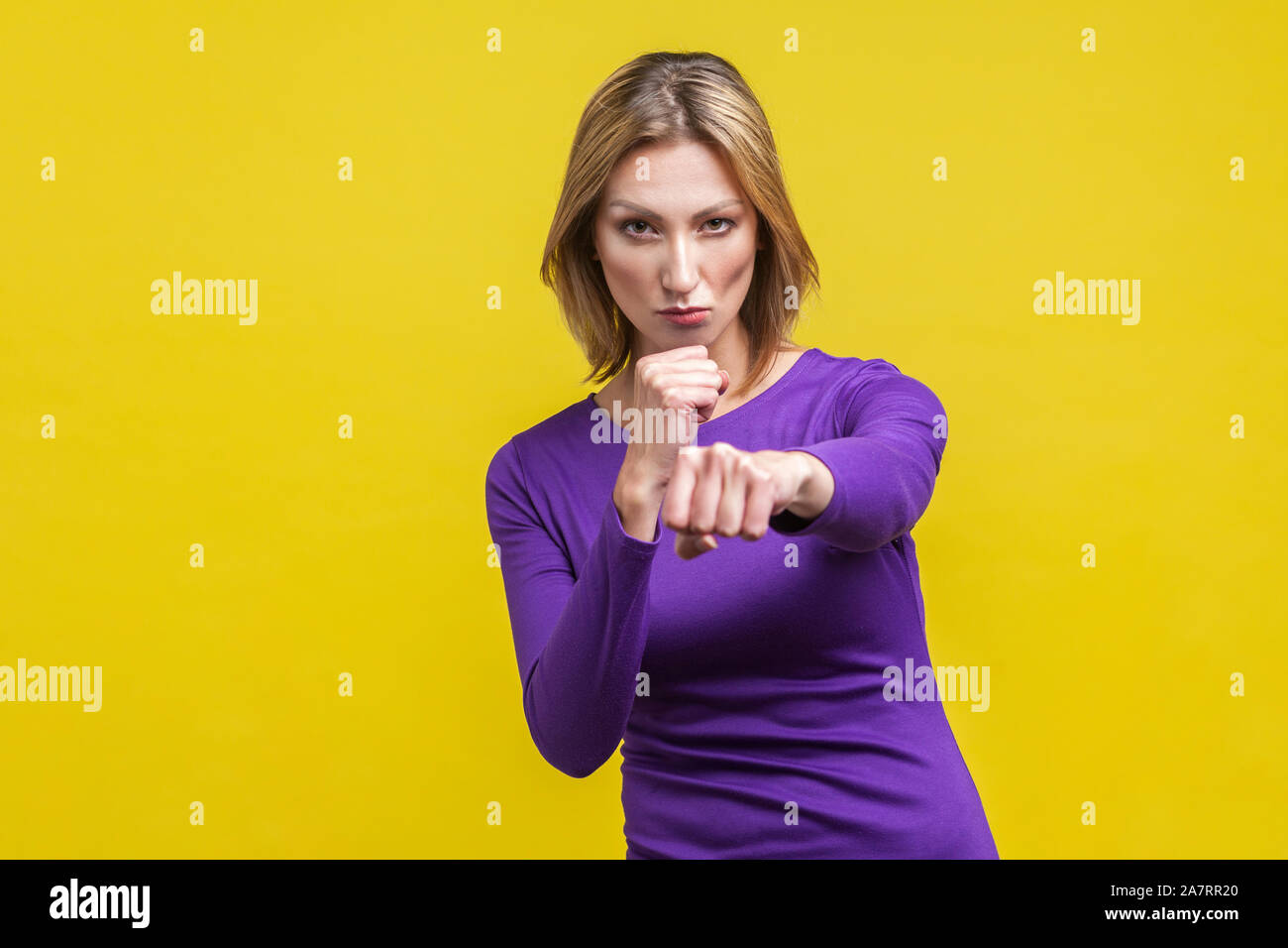 Portrait of confident purposeful businesswoman in purple dress standing holding clenched fists ready to boxing, strong spirit to fight for the goal. i Stock Photo