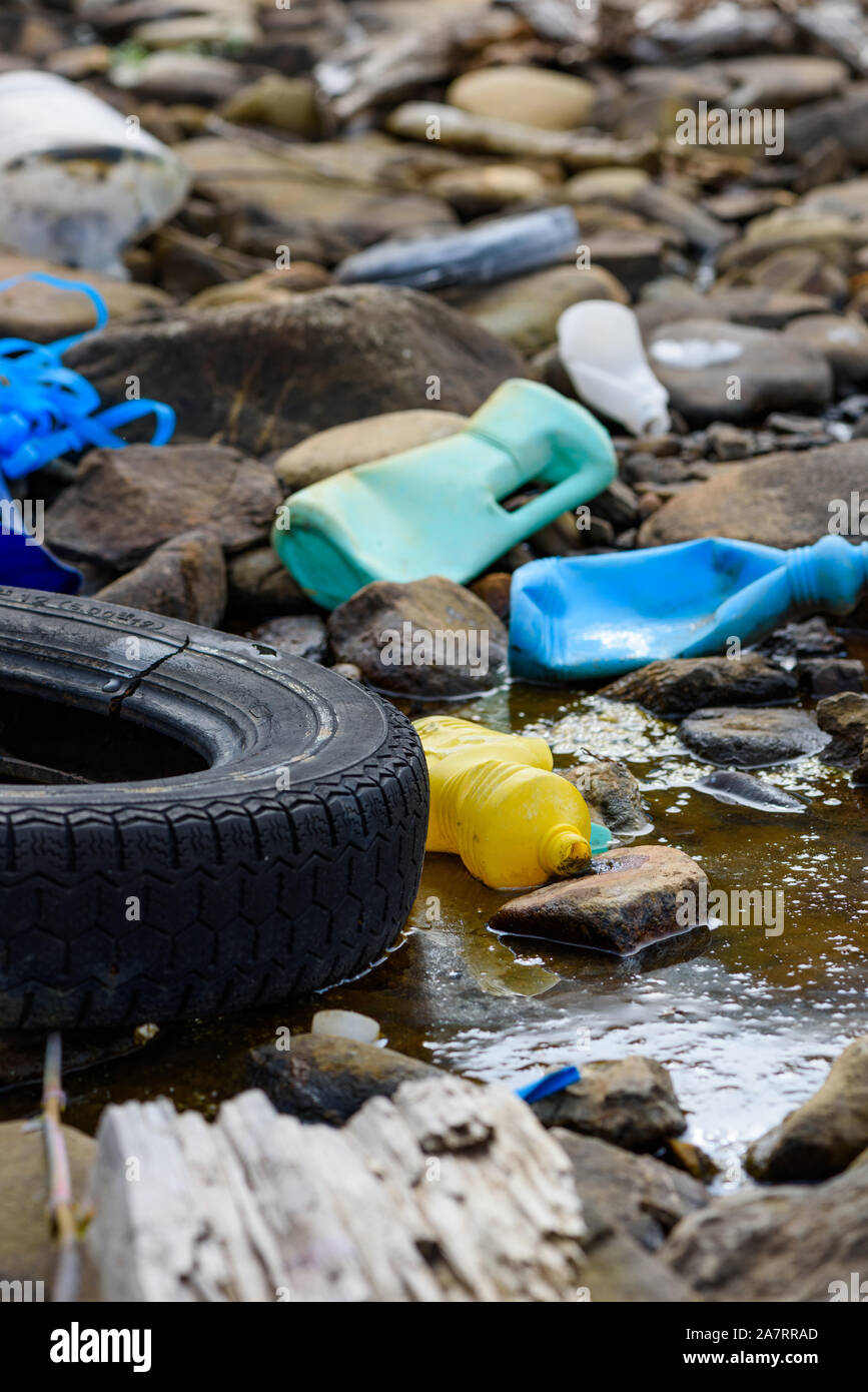 Enviromental pollution. Rubber tire with plastic bottles and waste in dirty water on ocean beach. Stock Photo
