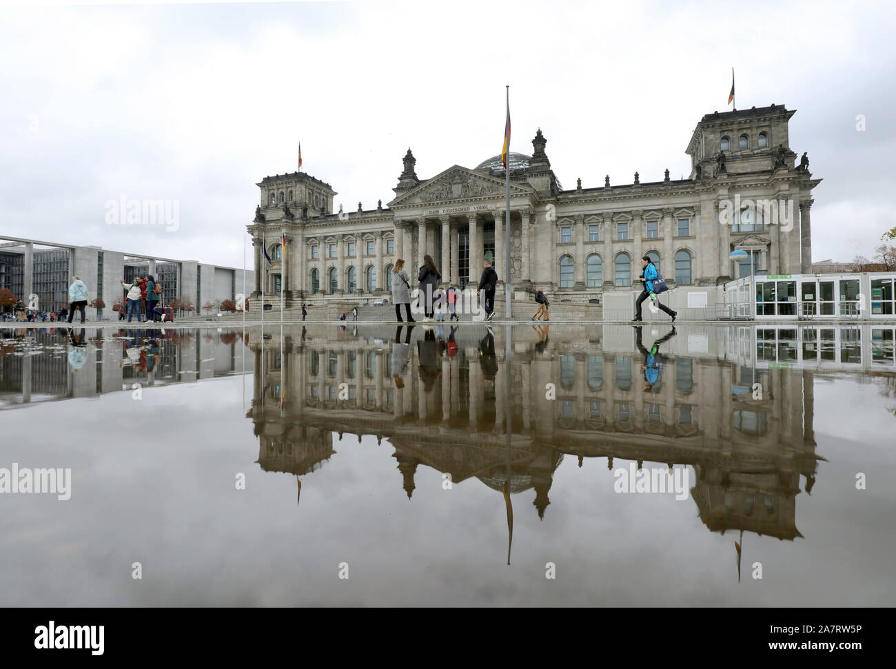 Berlin, Germany. 04th Nov, 2019. People walk past a puddle of rain in front  of the Reichstag building in the government district, where the seat of the  German Bundestag is reflected. Credit: