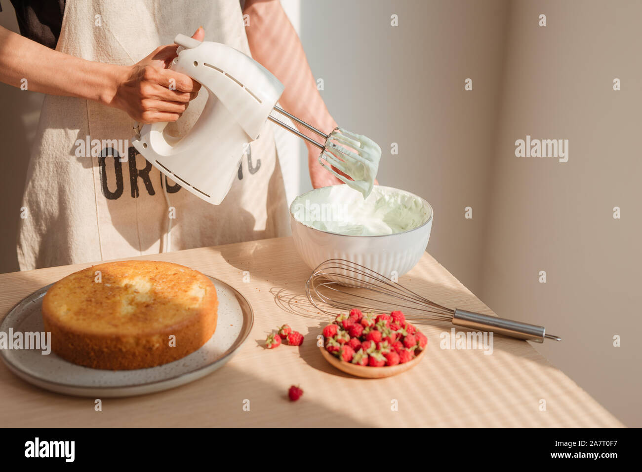 Male hands whipping whites cream in glass bowl with mixer on wooden table. Making sponge cake or red velvet cake Stock Photo