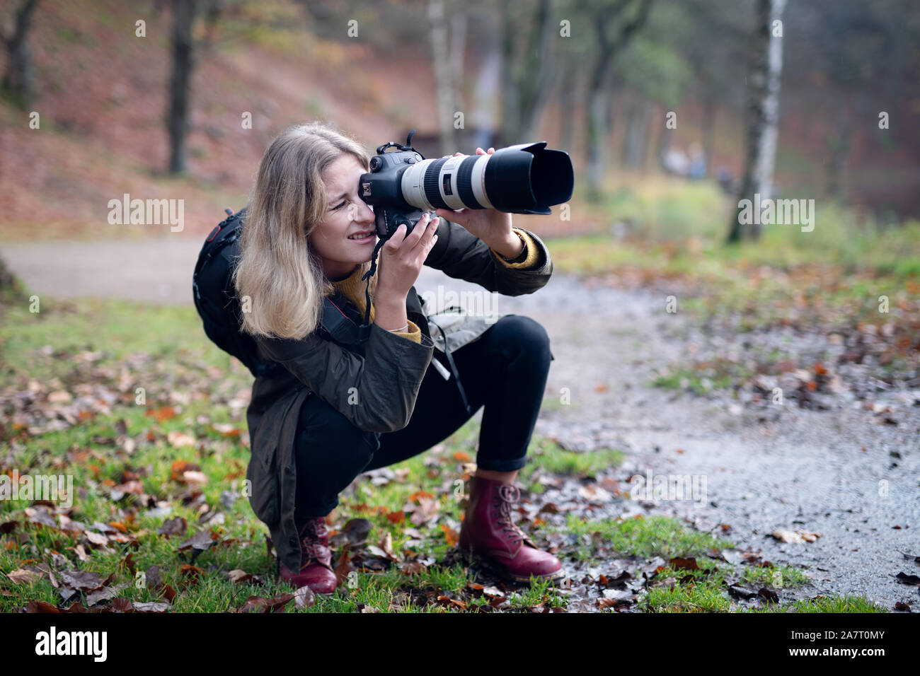 Blonde photographer squatting and using camera with large telephoto lens while taking shots in nature Stock Photo