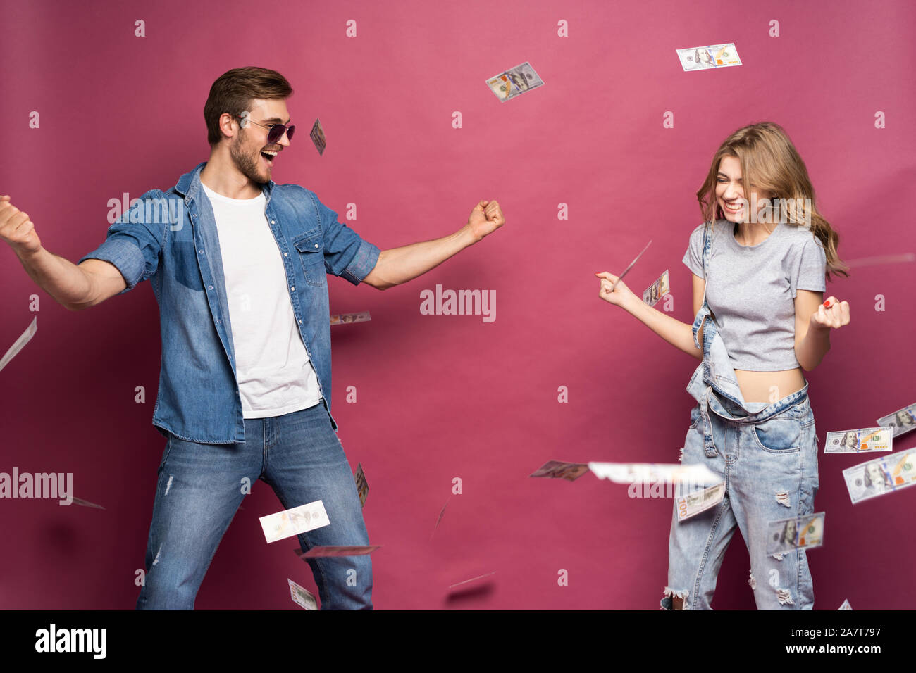 Portrait of a happy smartly dressed couple celebrating while standing under money shower isolated over pink background. Stock Photo