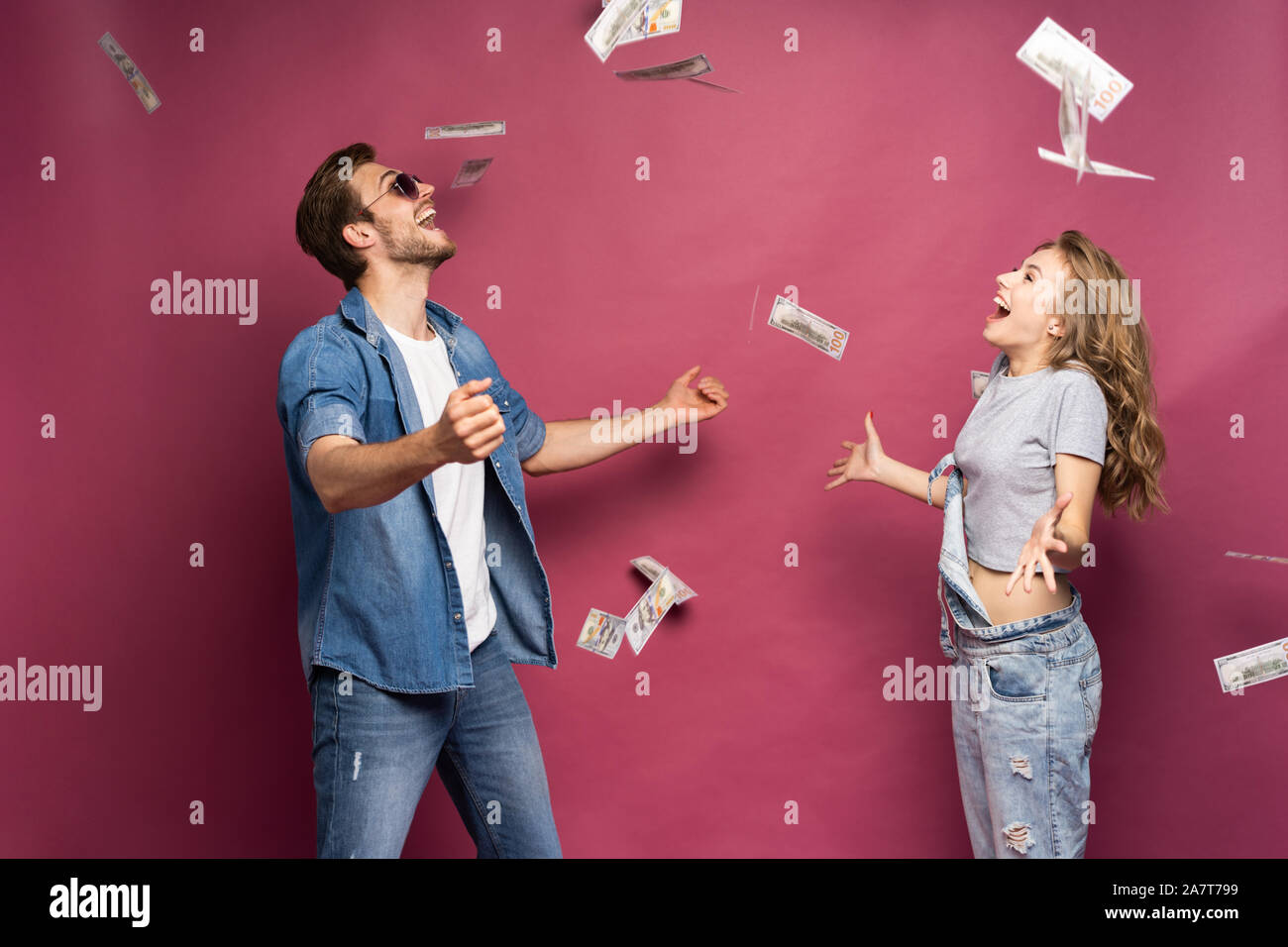 Portrait of a happy smartly dressed couple celebrating while standing under money shower isolated over pink background. Stock Photo