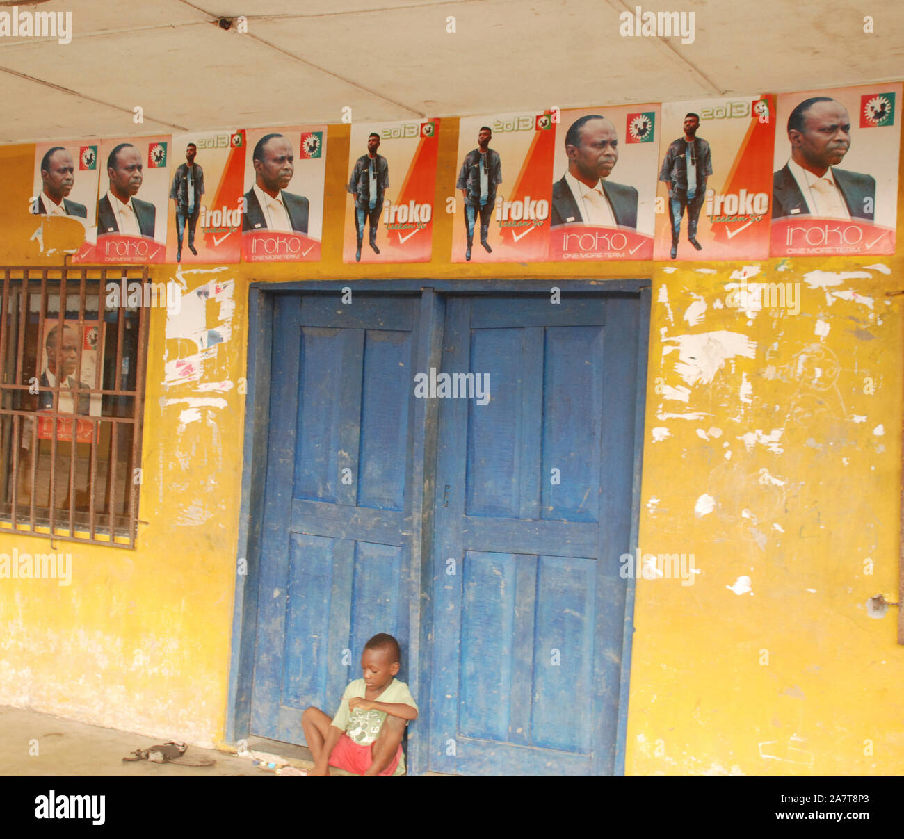 A boy sitting under the Governor's Poster at Ayetoro poor community of Ondo State, Nigeria. Stock Photo
