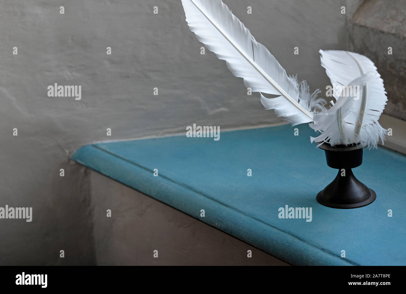 white feather quills in inkwell on blue painted shelf Stock Photo