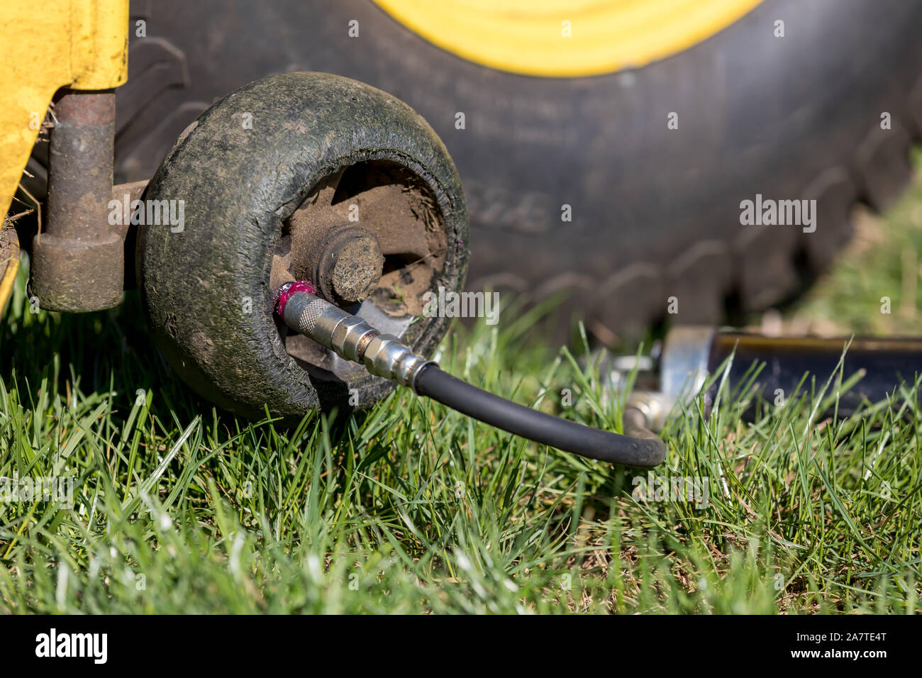 Lawnmower deck height gauge wheel bearing being lubricated with grease gun. Concept of home and lawn equipment maintenance and repair Stock Photo