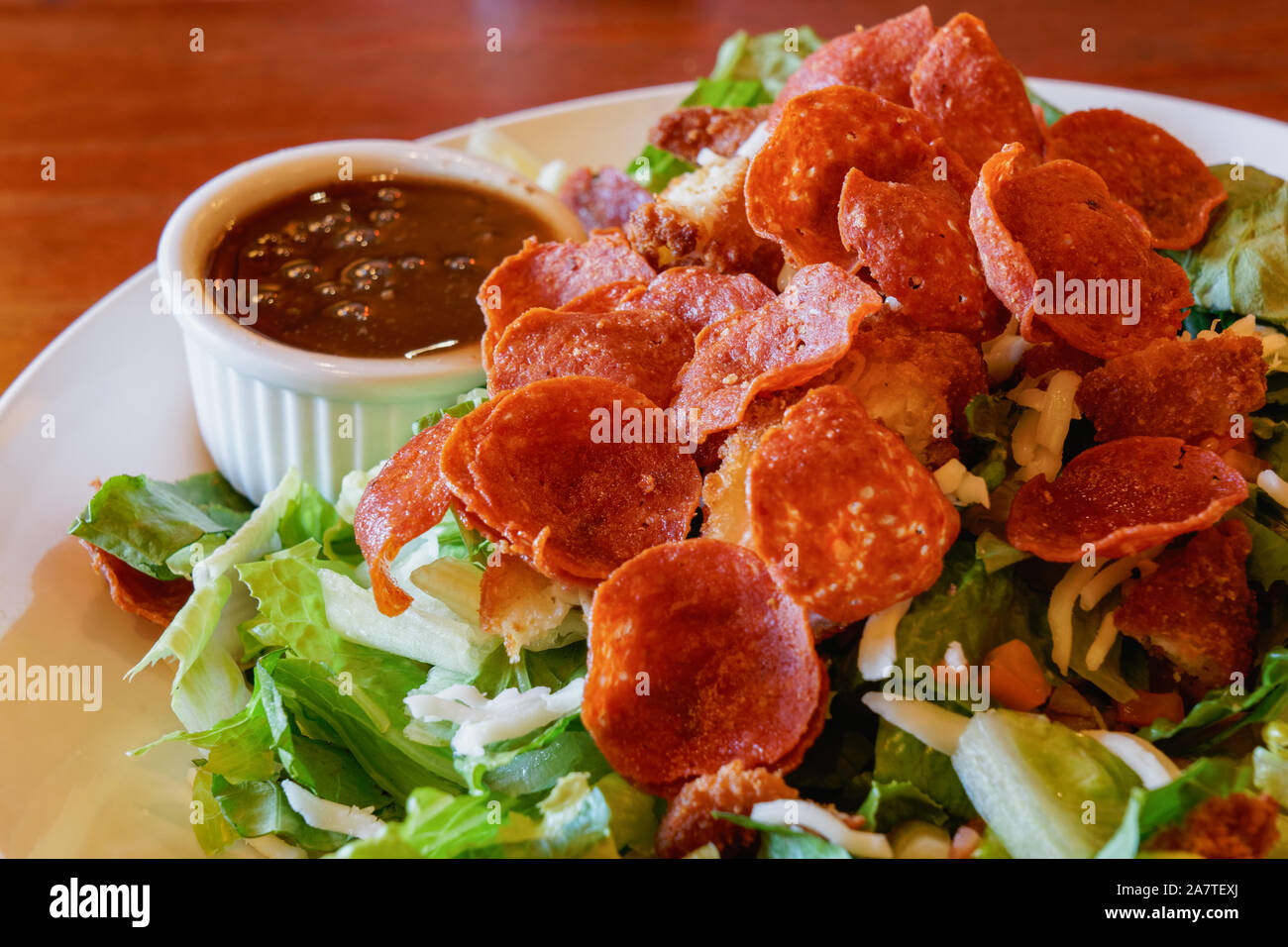 fried pepperoni on top of a salad with a side of balsamic dressing