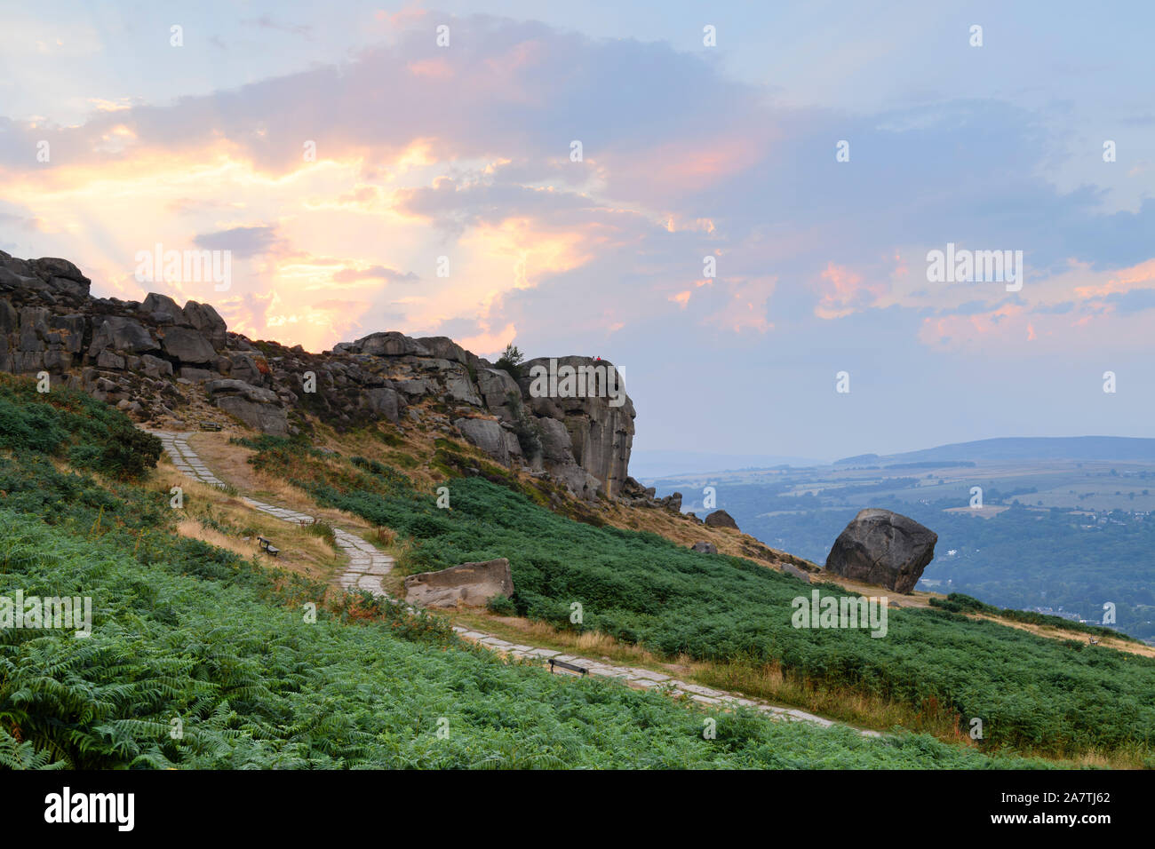 Rural scenic landscape (dramatic colourful sunset sky, sun rays, high rocky outcrop, valley) - Cow & Calf Rocks, Ilkley Moor, Yorkshire, England, UK. Stock Photo