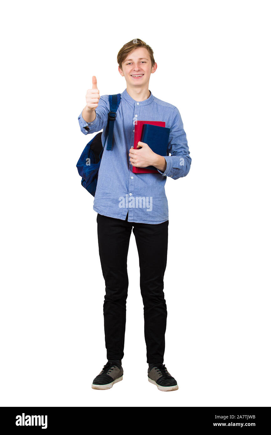 Full length portrait of young student boy holding two books to chest and carrying his backpack on the way to school. Teenager showing thumb up positiv Stock Photo