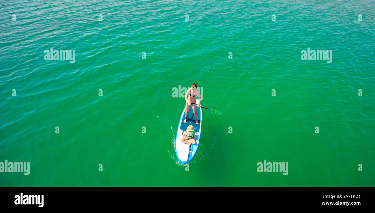 Little girl in a life vest sitting on the paddle board with mother