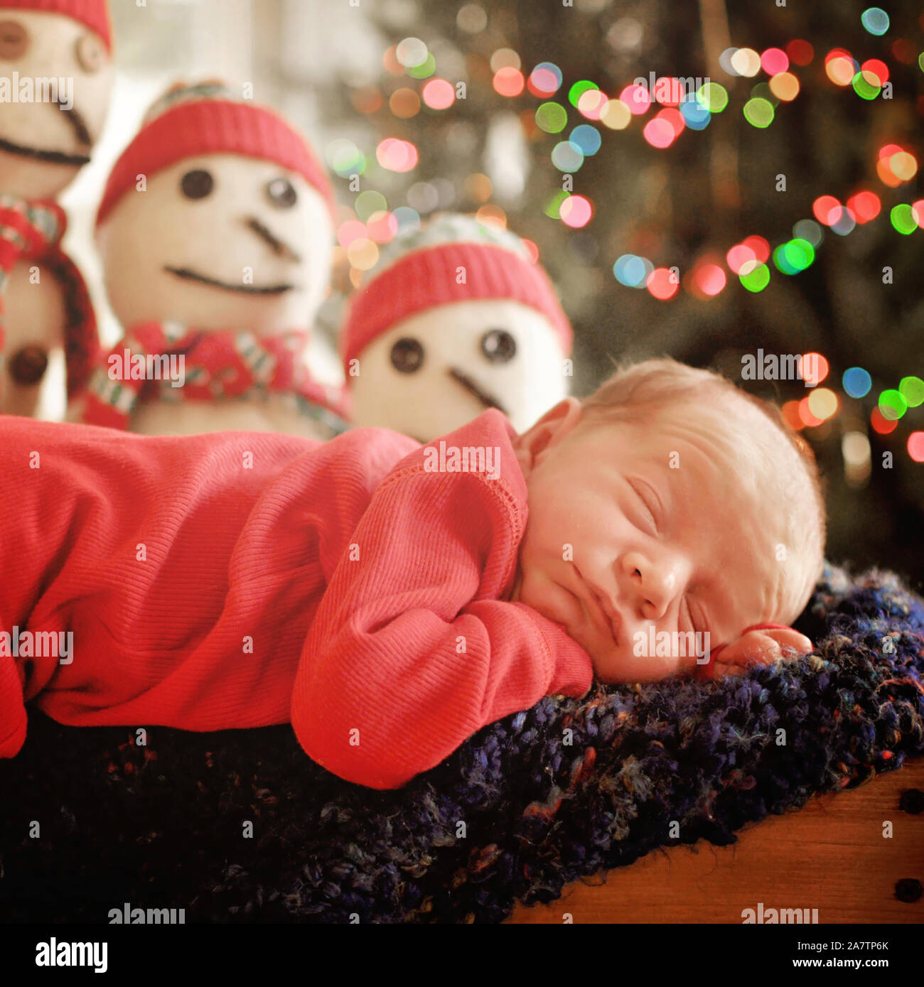 Newborn Christmas baby boy sleeping on afghan with light bokeh and snowmen in background Stock Photo