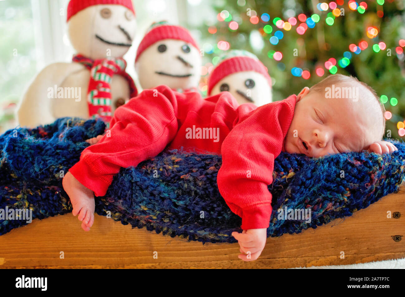 Newborn Christmas baby boy sleeping on afghan with light bokeh and snowmen in background Stock Photo