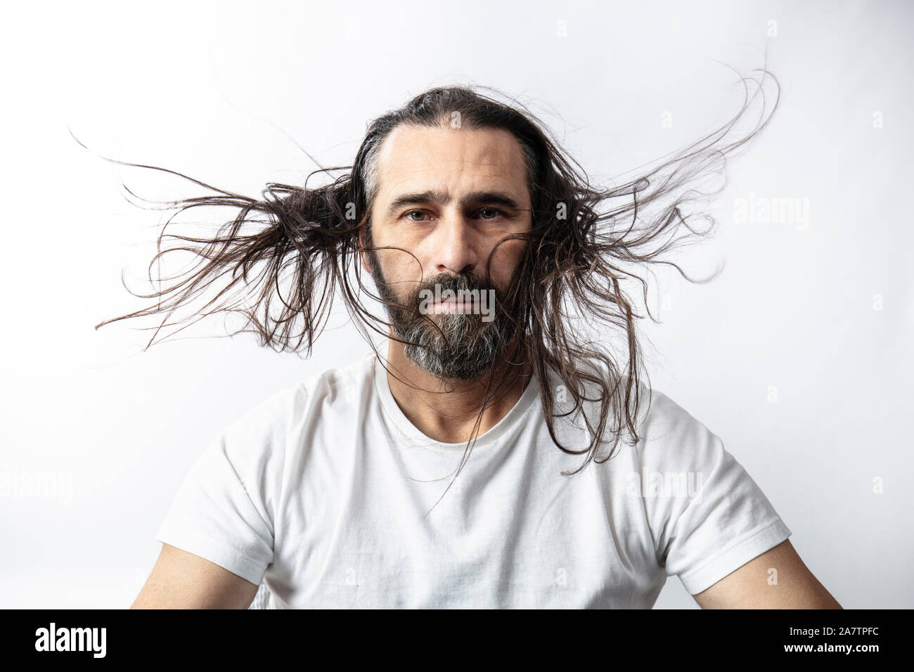 portrait of a caucasian man with beard and fluttering long hair. Serene expression and look at the camera. Stock Photo