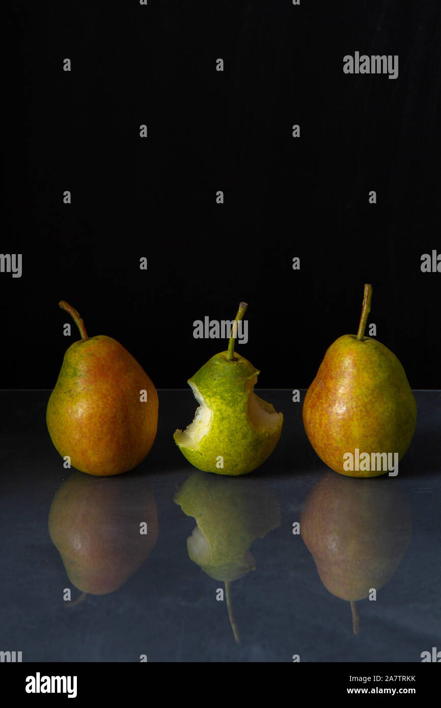 Three ripe pears of yellow, green and red color lie on a gray glossy table on a black background. Pears are reflected in the surface of the table. One Stock Photo