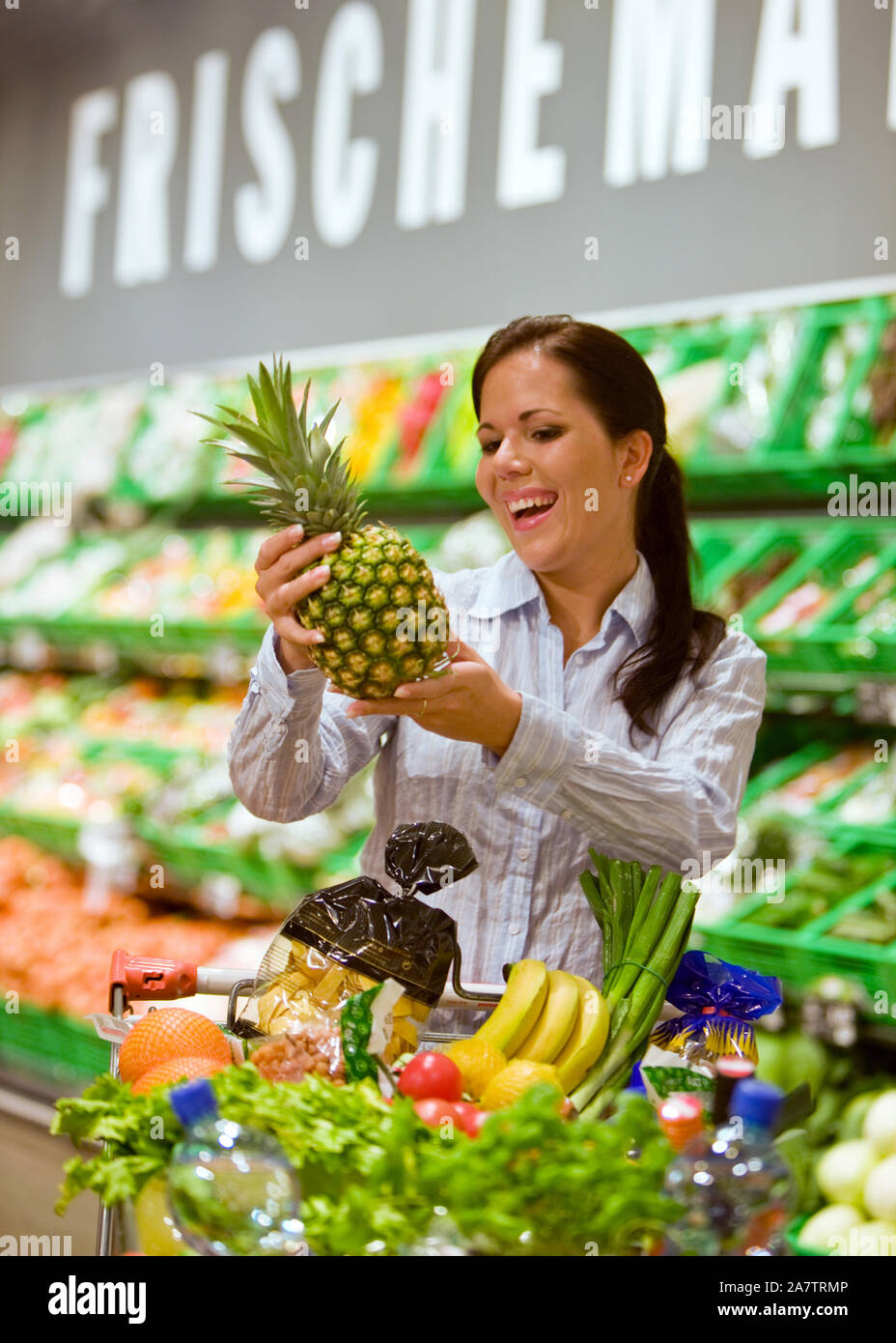 Frau geht Einkaufen im Supermarkt, kauft eine Ananas, Einkaufswagen mit Obst, Gemüse und Lebensmittel,  MR: Yes Stock Photo