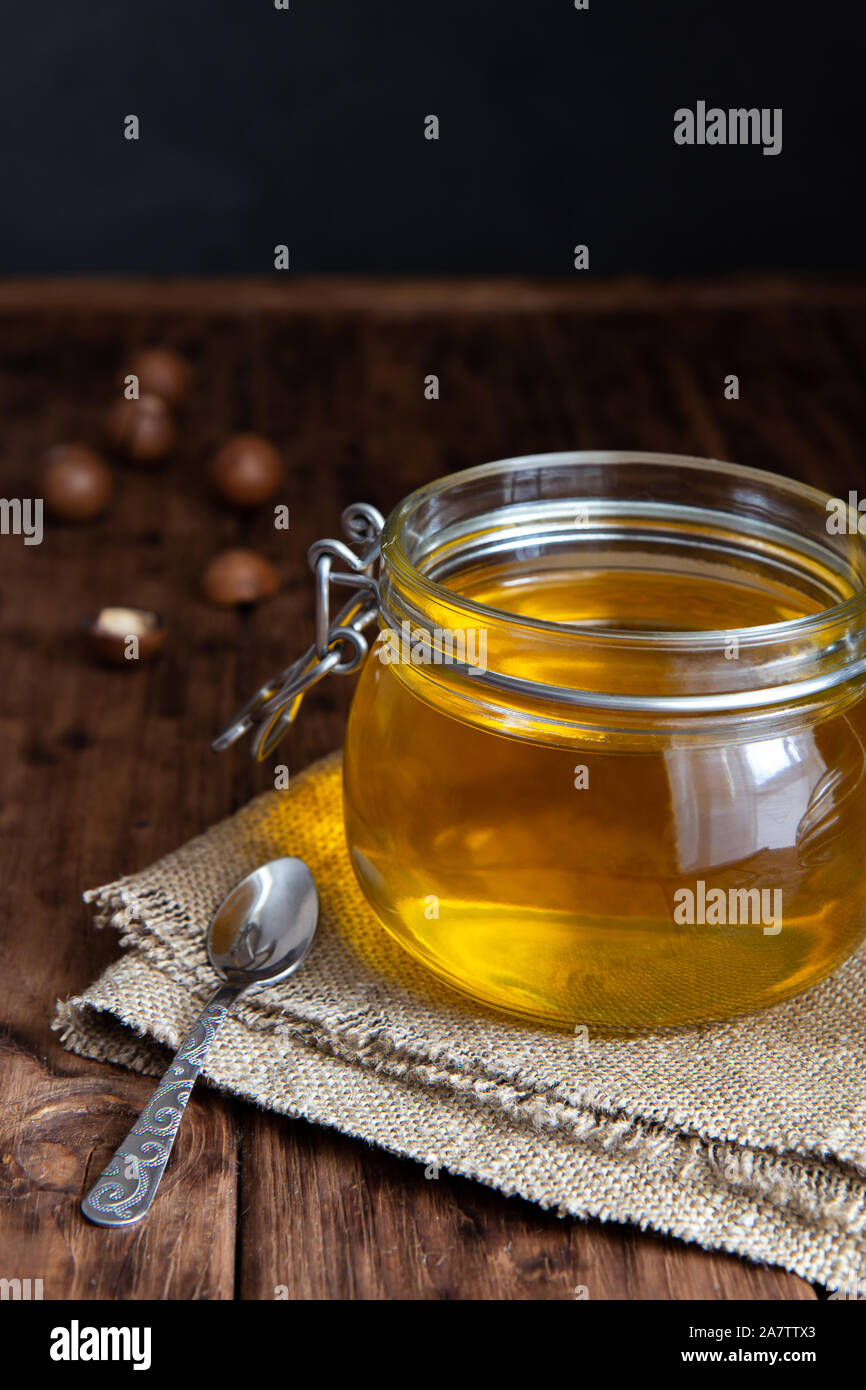 Jar of clarified ghee butter on a wooden table. Burlap, macadamia nuts ...