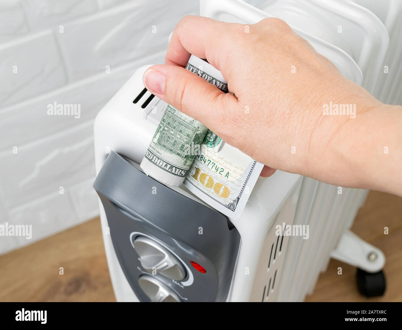 Woman hand putting one hundred dollar bill into home electric oil heater. The concept of higher