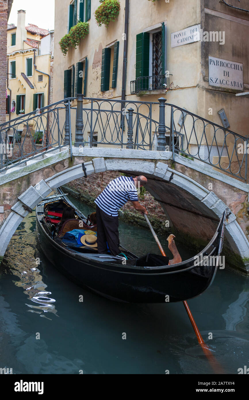 Gondolier ducks under the stone arch of the Ponte dei Carmini, Rio San