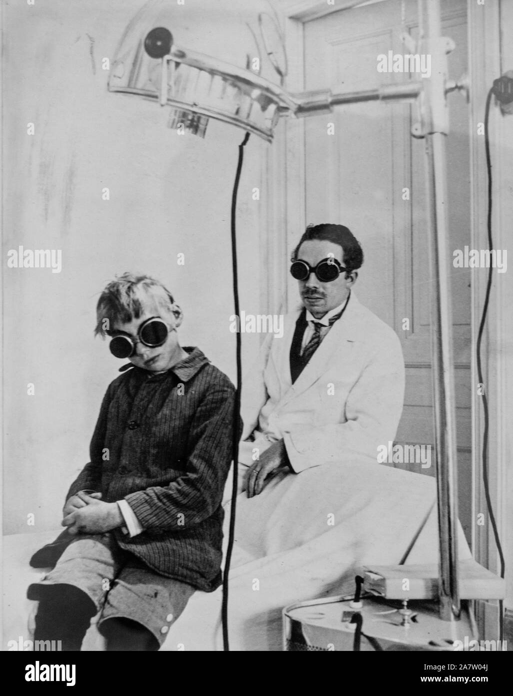 1930 photograph showing doctor and child patient with goggles during light therapy / phototherapy session in clinic Stock Photo
