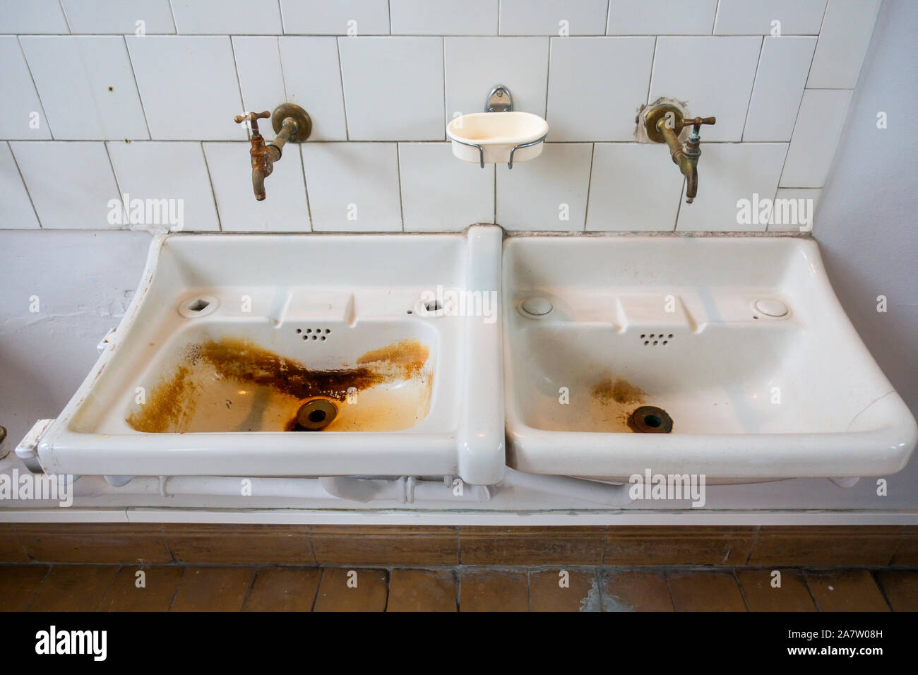 Two dirty sinks / wash basins covered in rusty stains in bathroom of disused clinic Stock Photo