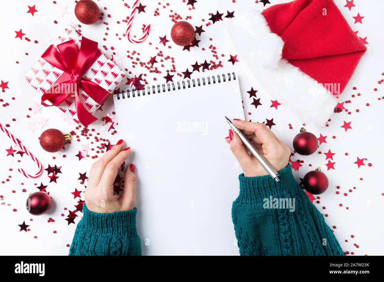Woman in green sweater writes checklist of plans and dreams for next year. Wish list for Christmas. To Do List for New 2020 year with red Holiday deco Stock Photo