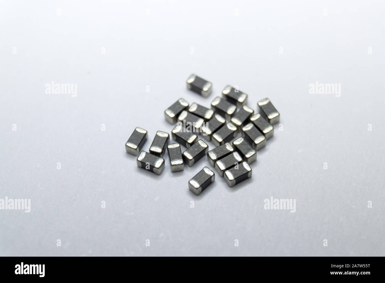 Abstract close-up of grey scattered 0402 SMT surface mount chip ferrite bead power electronics components on white background in random pattern Stock Photo