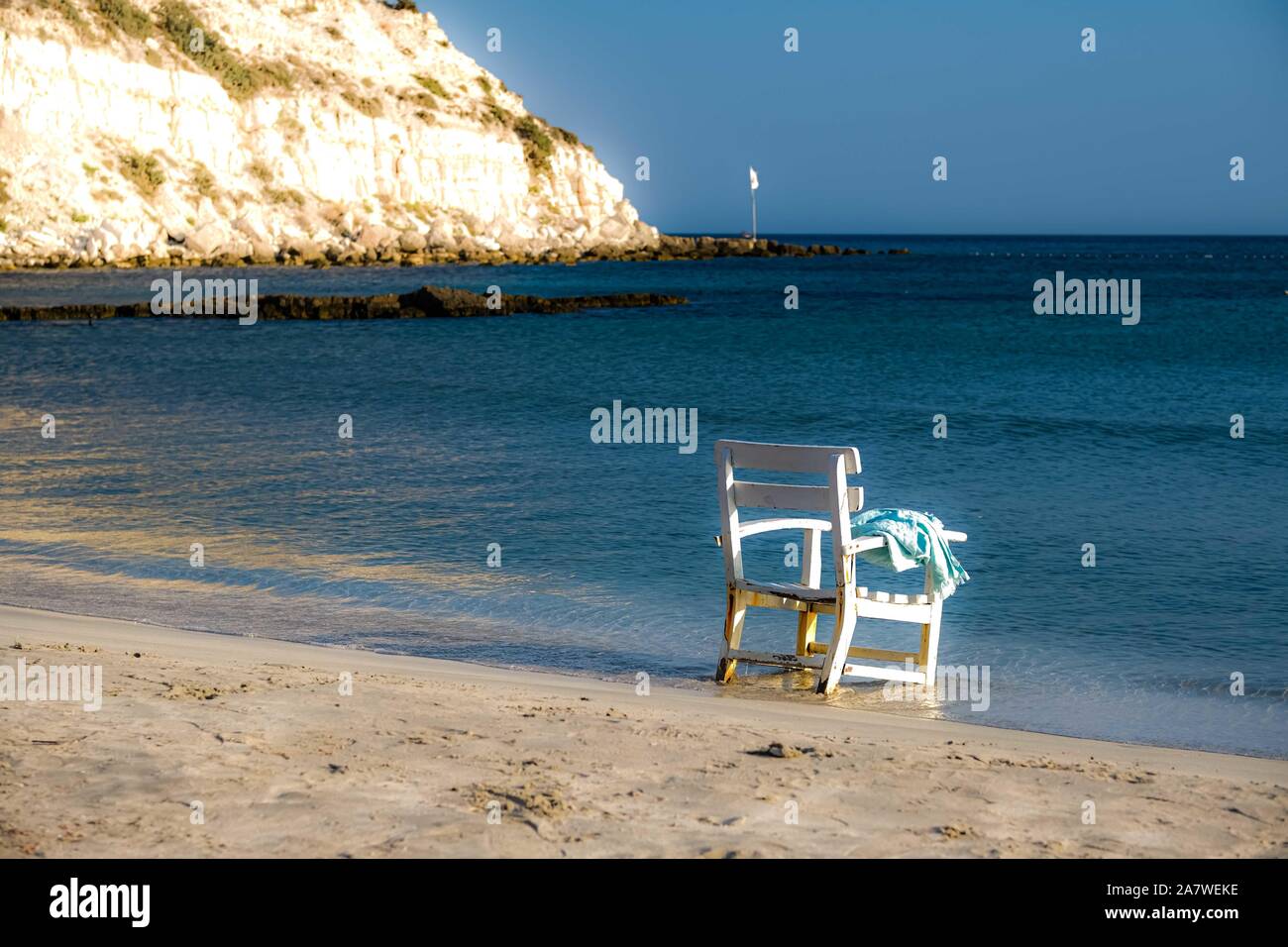 Lonly shabby white chair and blue towel left at the armrest facing the blue Mediterranian sea. Solitude concept. Cesme, Izmir, Turkey. Space for text. Stock Photo