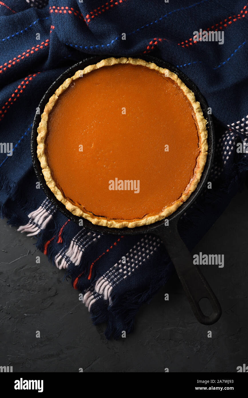 Hygge still life concept. Homemade pumpkin pie in cast iron pan on woolen cloth on black background top view copy space Stock Photo