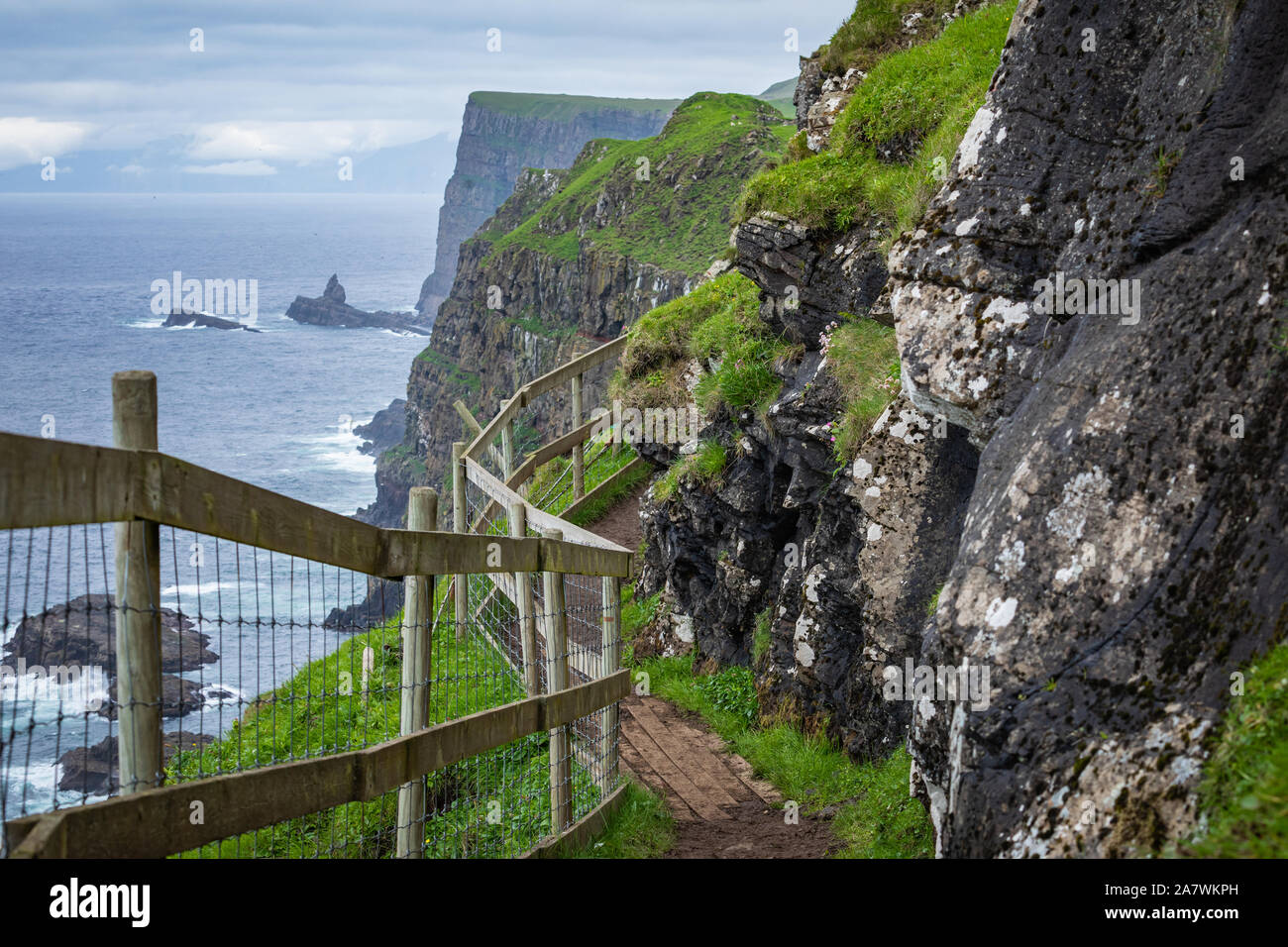 View on the Mykines island with moody clouds covering the top of the mountains and sheep grazing on the pasture, Mykines island, Faroe Islands, Europe - Stock Image