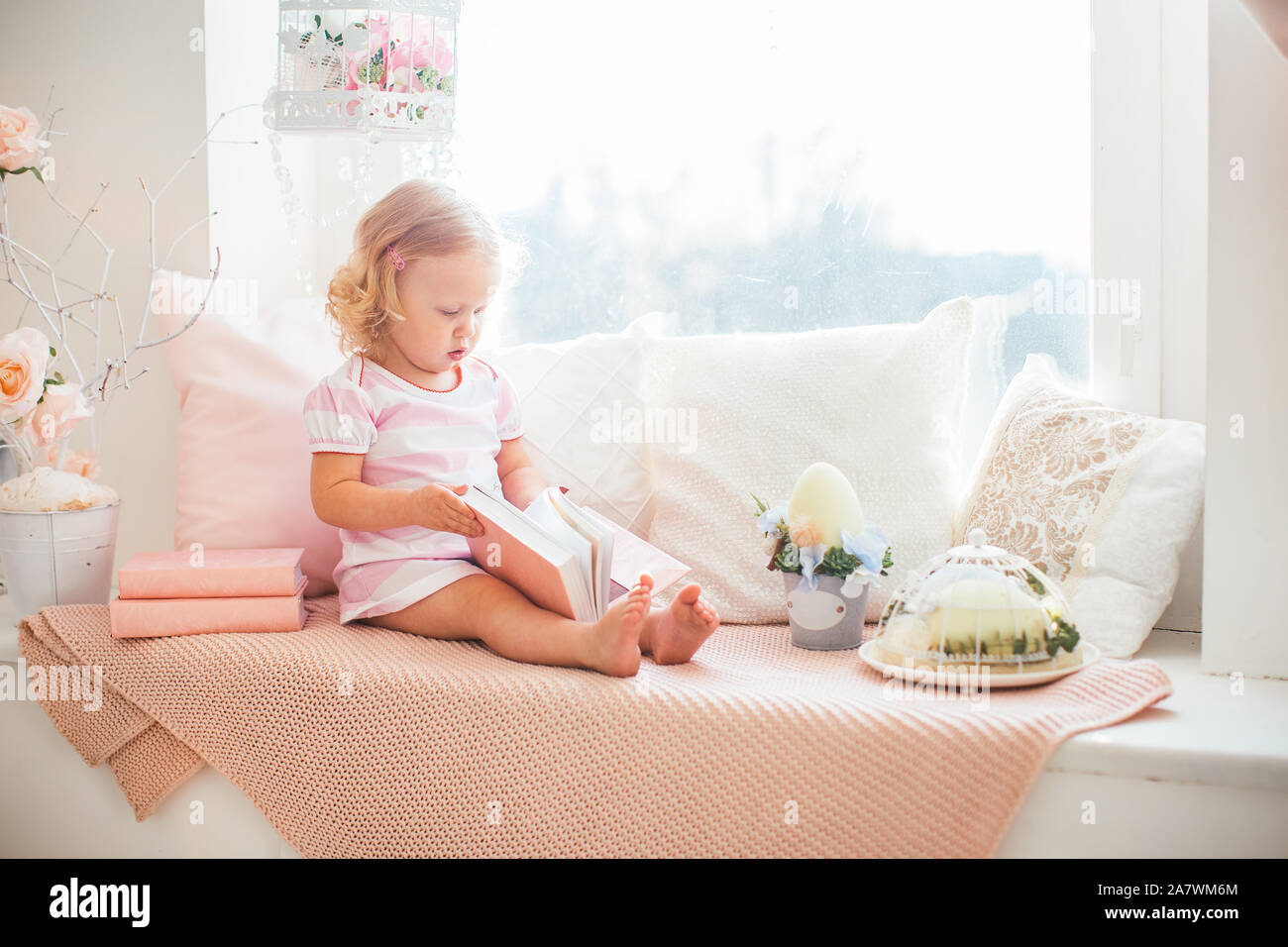 Cute little curly blonde girl in a pink dress with a book on a ...