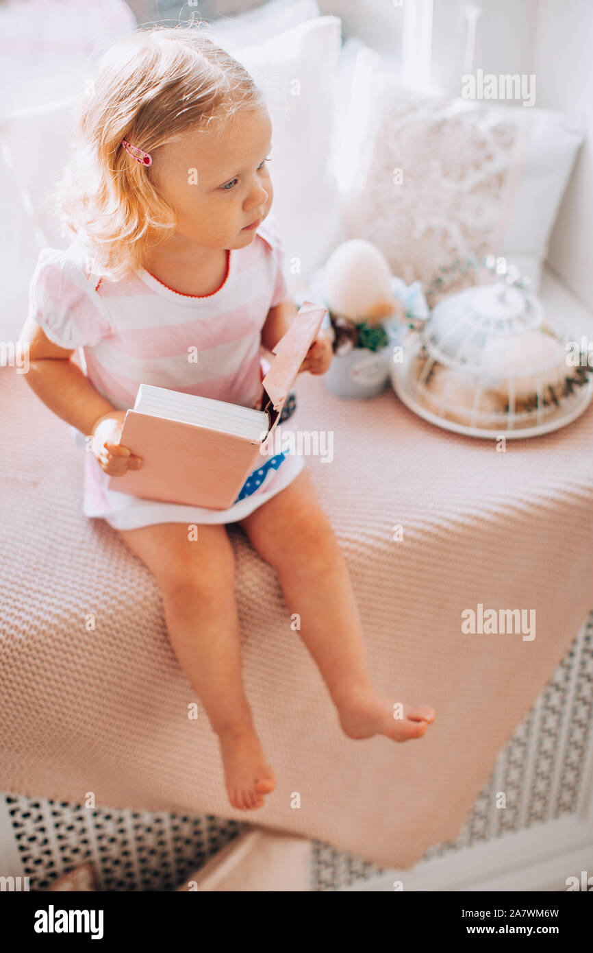 Cute little curly blonde girl in a pink dress with a pink book on a ...