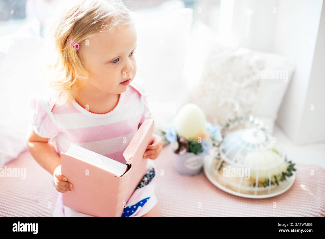 Cute little curly blonde girl in a pink dress with a pink book on a ...
