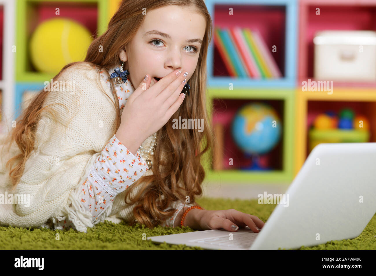 Emotional cute girl using laptop while lying on floor with green carpet ...