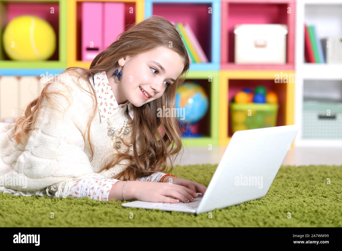Emotional cute girl using laptop while lying on floor with green carpet ...