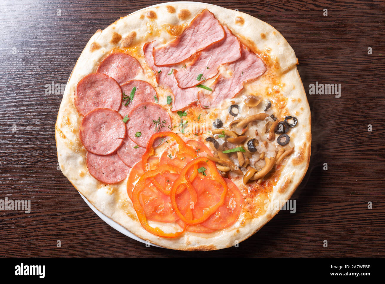 Cheap pizza 4 seasons. With ham, pepperoni, mushrooms, and tomatoes. Stock Photo