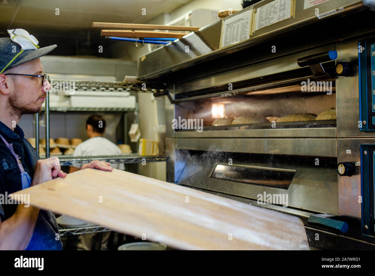 A baker places a tray of bread into oven in a commercial kitchen Stock Photo