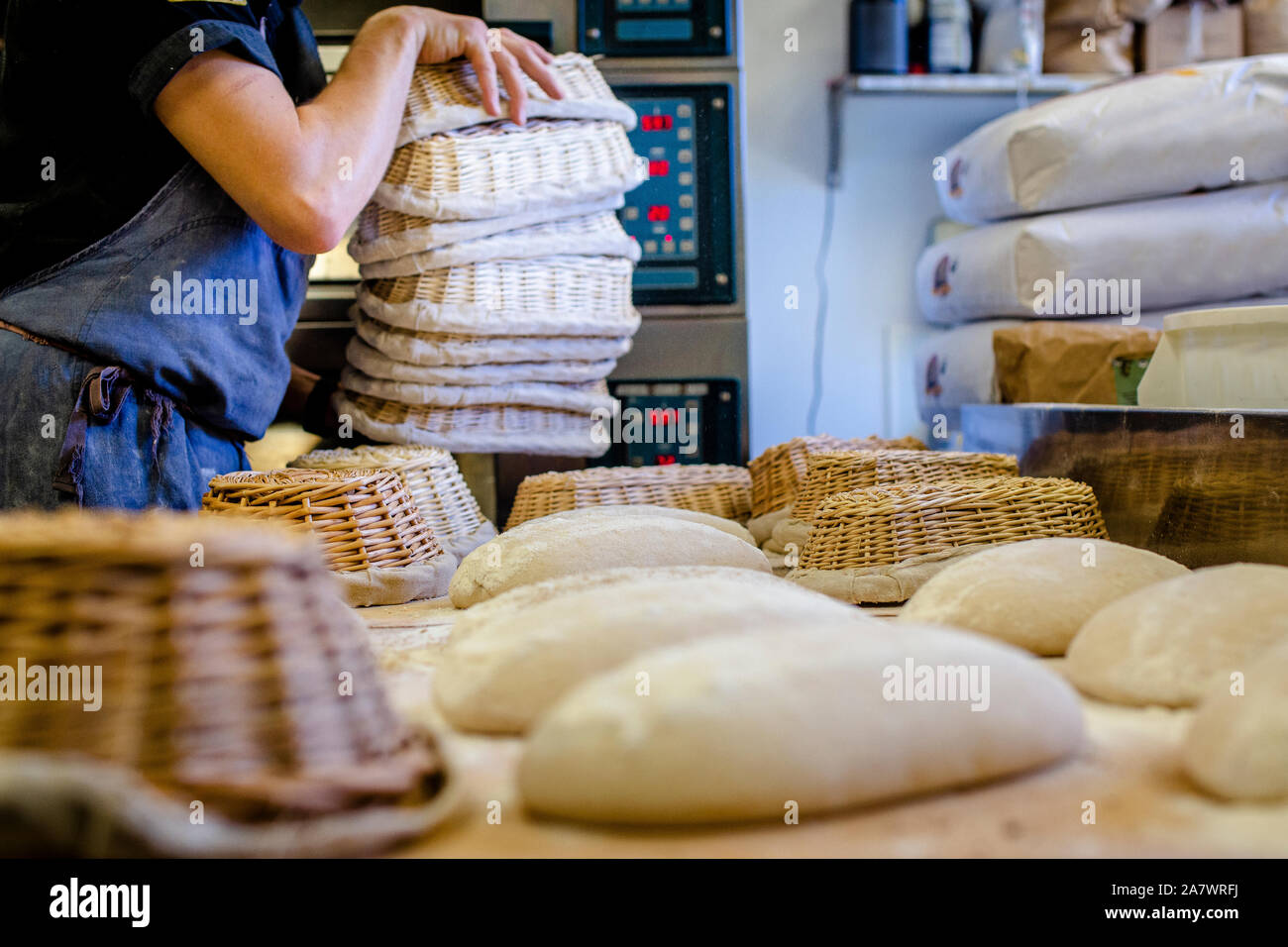 A professional baker with a stack of baskets places bread on counter