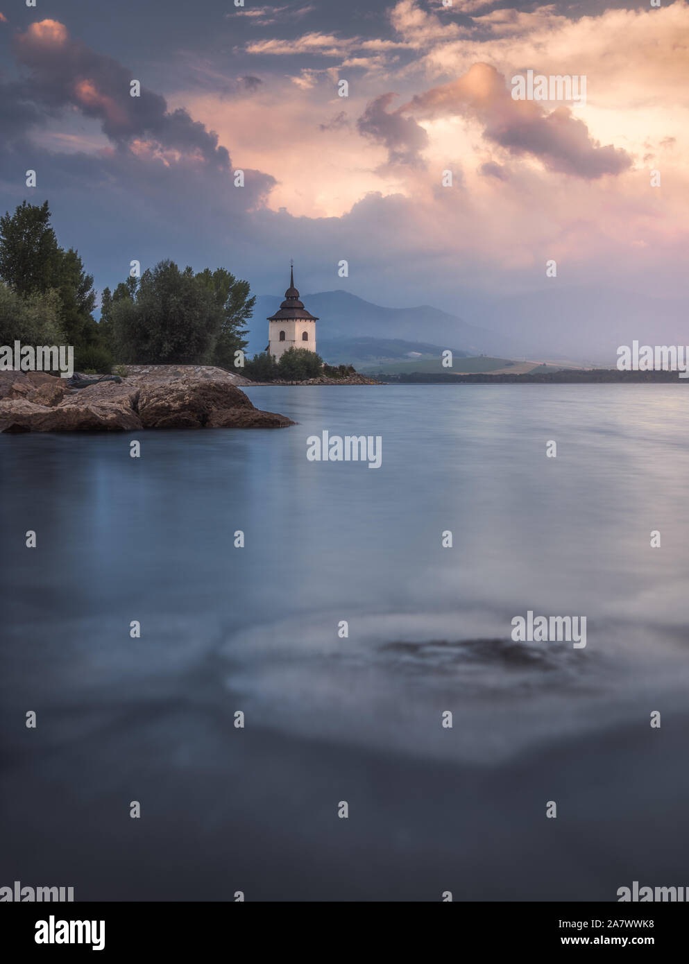 Virgin Mary Church by Liptovska Mara Lake with Western Tatras Mountains in Background at Sunset in Slovakia Stock Photo