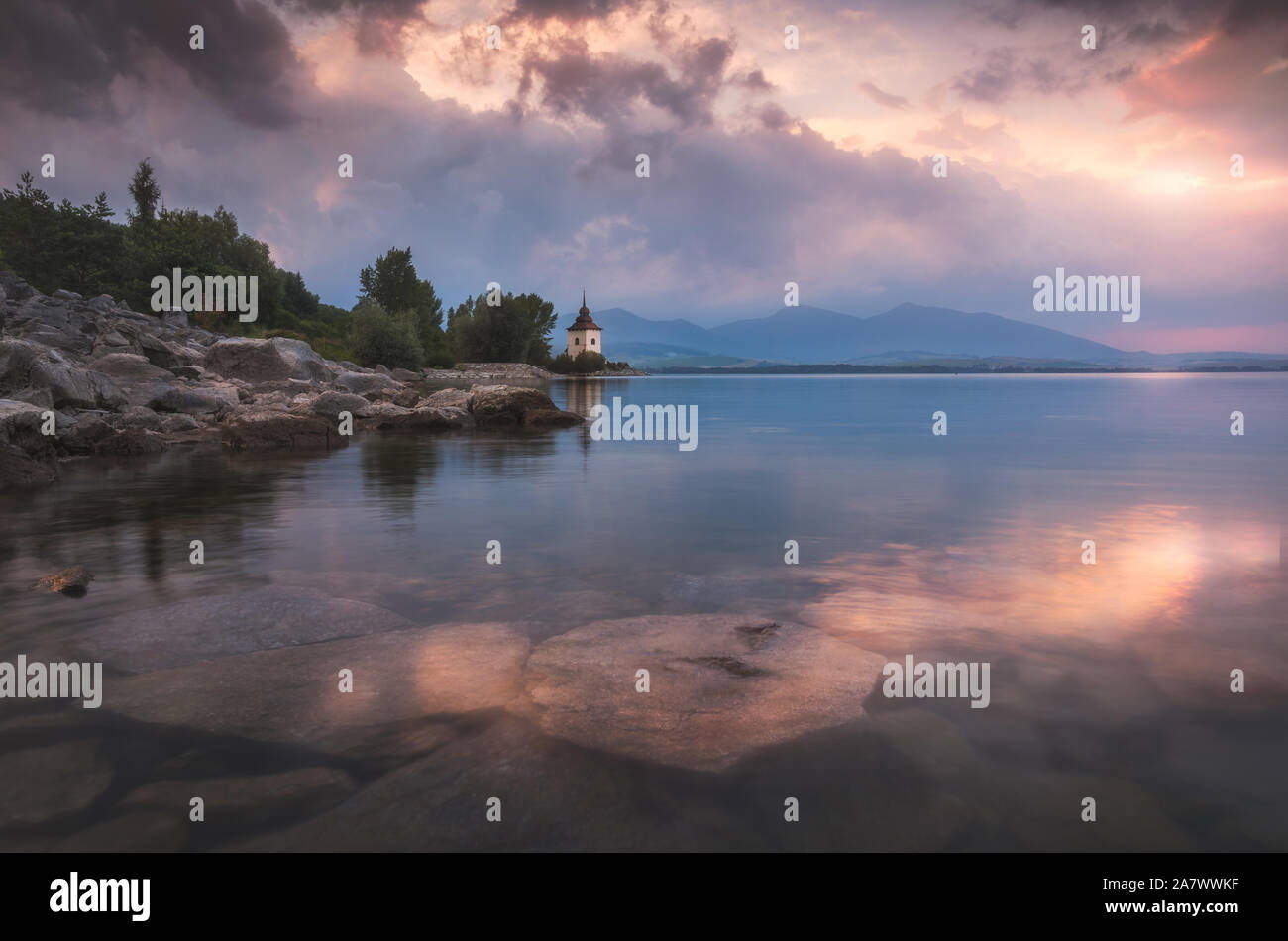 Virgin Mary Church by Liptovska Mara Lake with Western Tatras Mountains in Background at Sunset in Slovakia Stock Photo