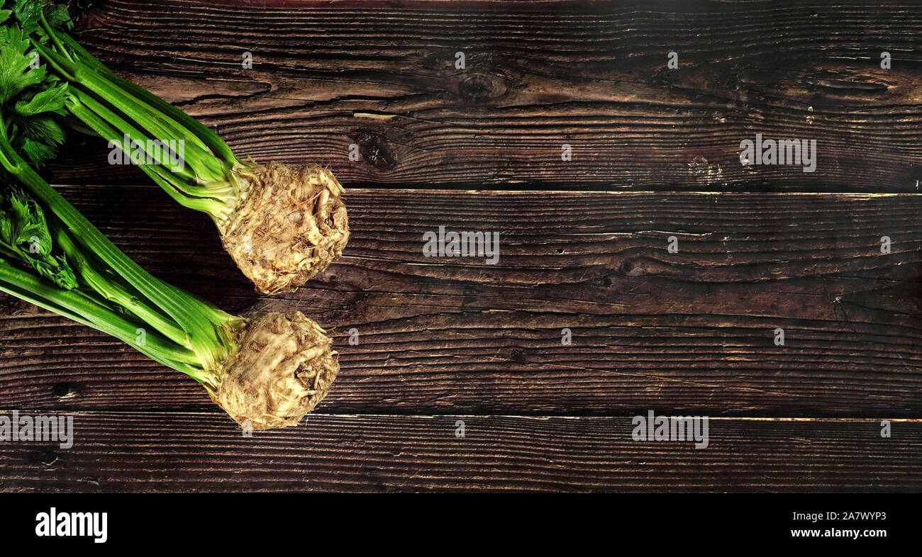 Celeriac root bulbs with green leaves on dark wooden board. Wide banner, space for text right side Stock Photo