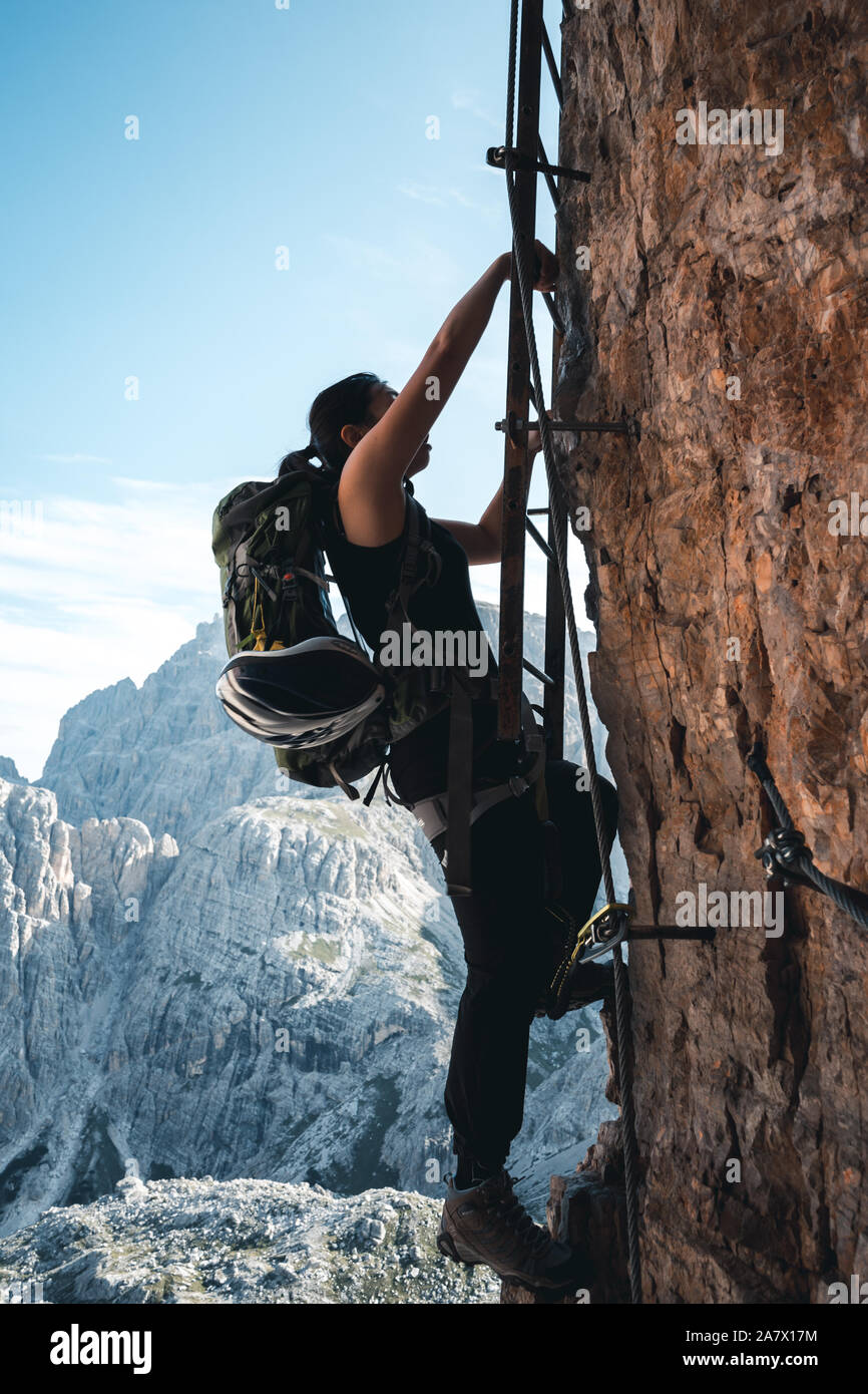 Girl climbs up a via ferrata letter on a massive wall at the Toblinger Knoten in the Dolomites, Italy Stock Photo