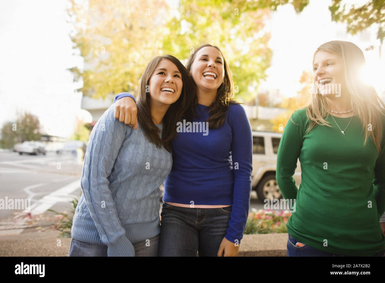 Three laughing young woman standing side by side on a suburban street. Stock Photo