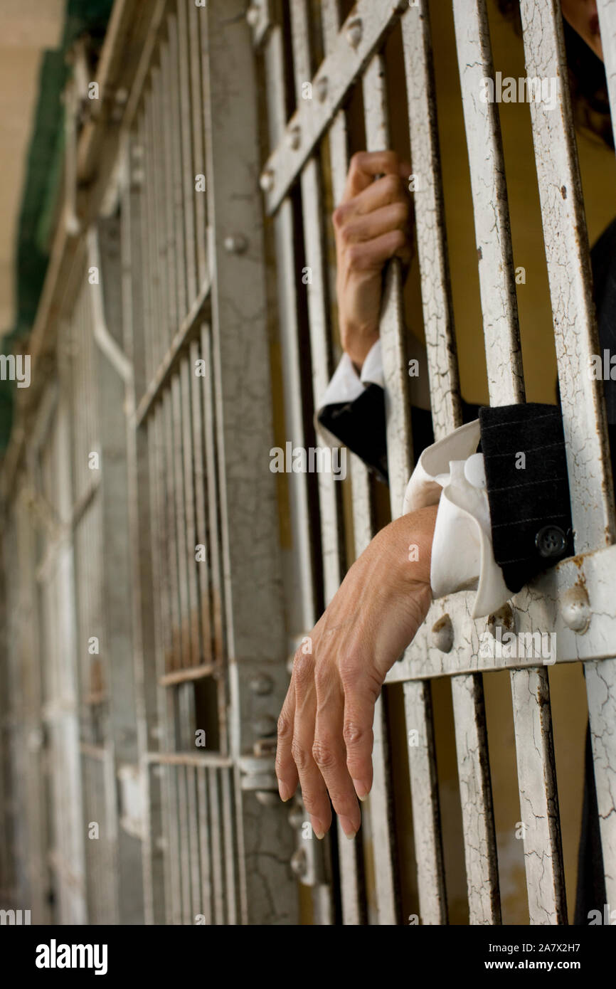 Hands of a mid-adult woman through bars of a prison cell in a derelict building. Stock Photo