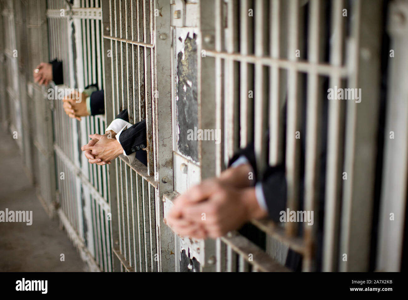 Hands of a mid-adult business woman and three colleagues through bars of a prison cell in a derelict building. Stock Photo